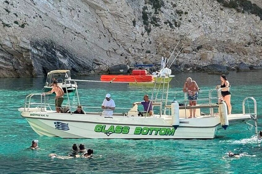Een boot genaamd 'GLASS BOTTOM' met passagiers en zwemmers in het water. 4