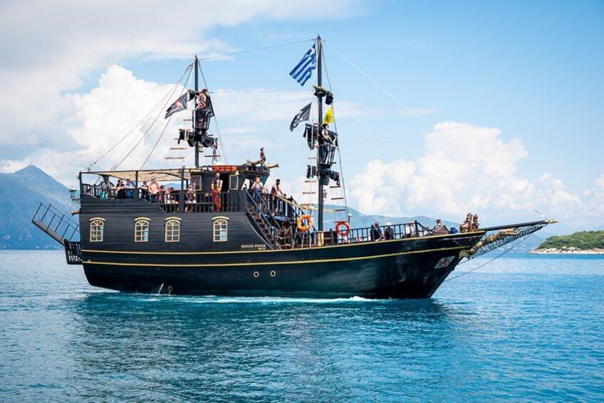Ein großes Segelschiff mit mehreren Decks und Flaggen fährt auf ruhiger See, im Hintergrund eine gebirgige Landschaft. 2