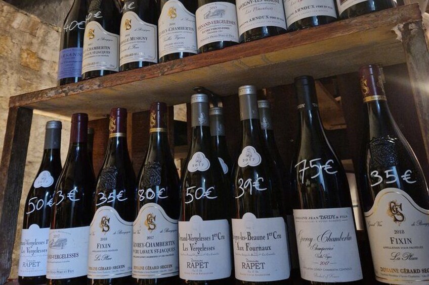 A collection of wine bottles with price tags on a wooden shelf. 2