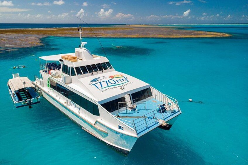 A white boat named 'T70 Ocean' with a blue deck, anchored in turquoise waters with a clear sky. 1