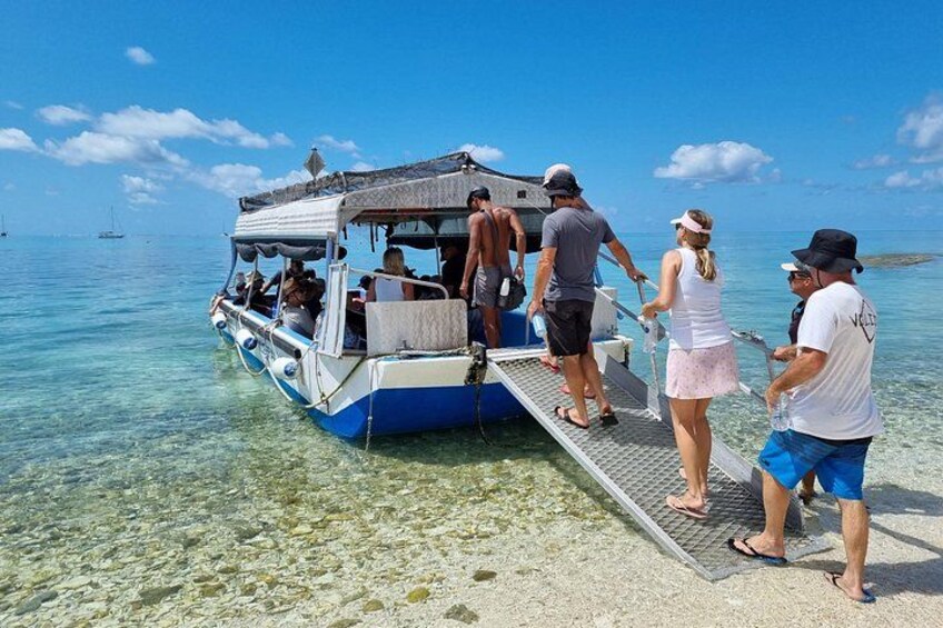 A boat with passengers boarding, clear blue water, and a distant island. 4