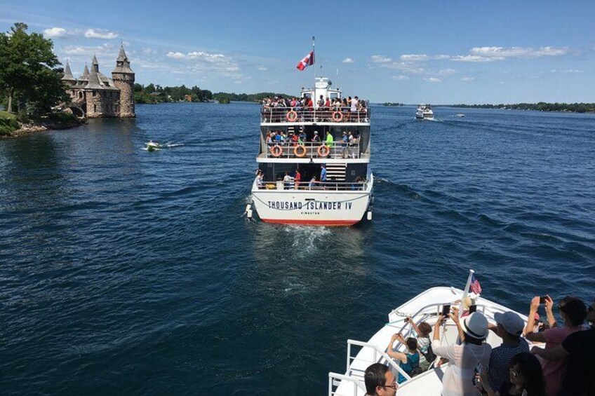 A large tour boat named 'Thousand Island IV' with passengers enjoying the view, a castle-like structure on the shore, and another boat in the background. 5