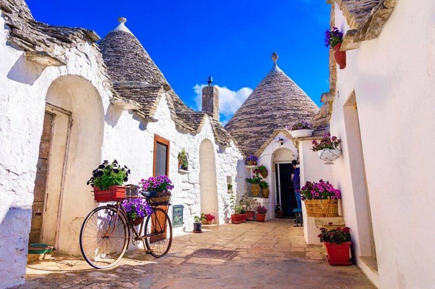 A narrow cobblestone street with white buildings, a bicycle, and potted plants. 2