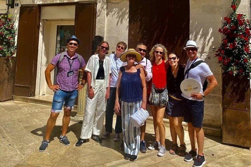 A group of people standing in front of a building with a door and windows, a potted plant, and a stone pavement. 5