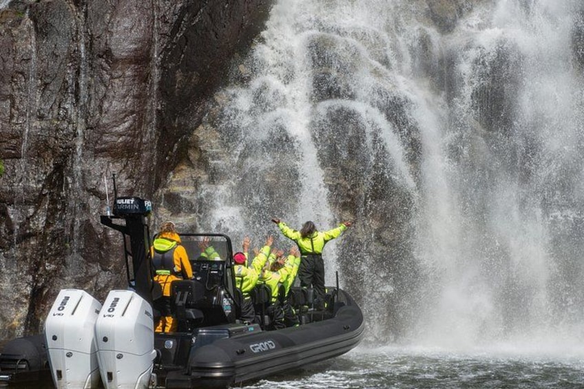 Ein Boot mit Personen in Sicherheitsausrüstung, ein Wasserfall im Hintergrund und eine felsige Klippe. 2