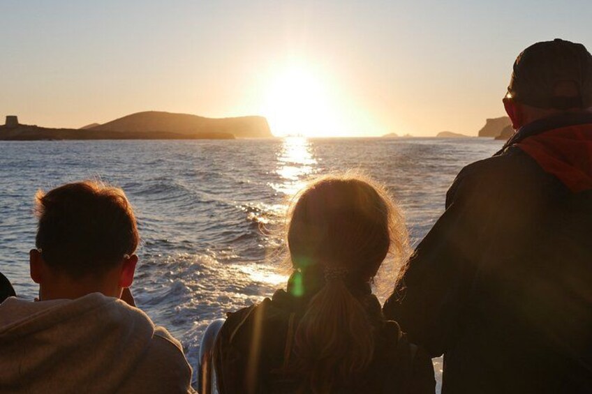 Three people on a boat during sunset, with the sun low on the horizon and reflecting on the water. 4