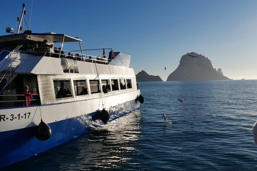 A boat with the registration number R-3-1-17 on calm waters, a clear sky, and a distant rocky island. 1