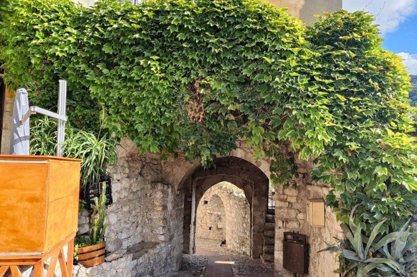 Un portail en pierre en arc de cercle, recouvert d’une luxuriante végétation de lierre, un chariot en bois et une plante en pot. 4