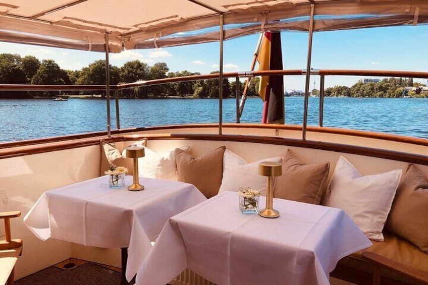 Interior de barco con dos mesas cubiertas con manteles blancos, cada una con una lámpara y un jarrón de flores. 5
