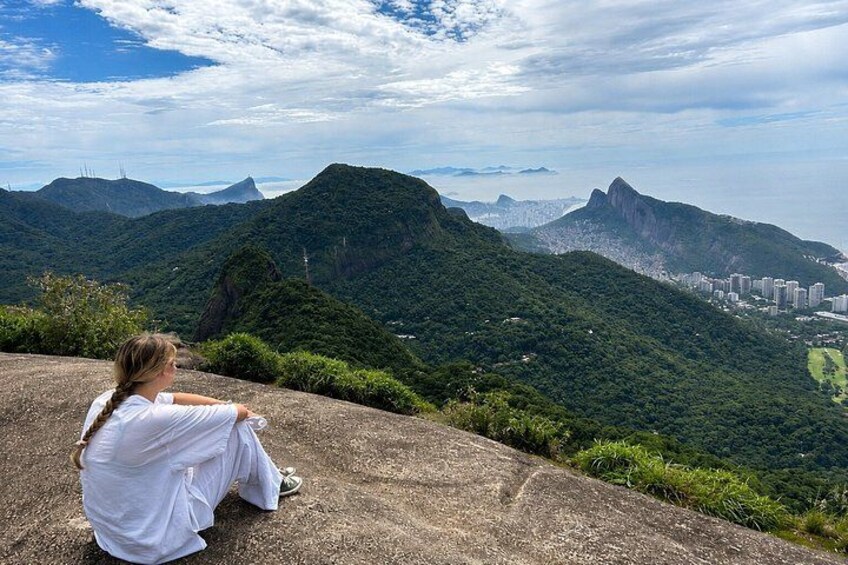 Eine Person sitzt auf einem Betonvorsprung und blickt auf eine gebirgige Landschaft mit einer Stadt in der Ferne. 2