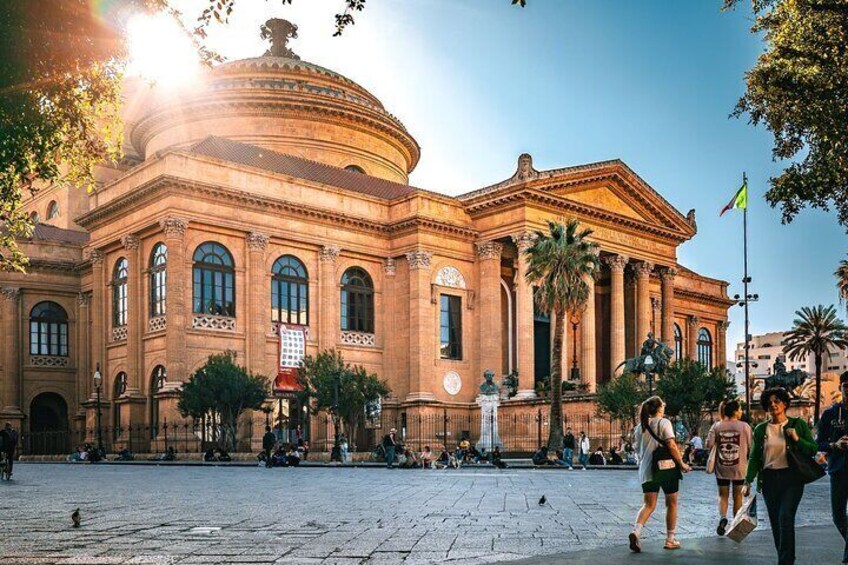 A historic building with a dome and columns, surrounded by a plaza with people and palm trees. 2