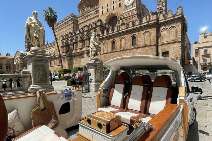 A convertible car parked in front of a historic building with statues and a clock tower. 1