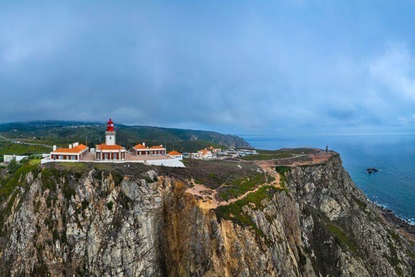A coastal lighthouse with a red top, situated on a rocky cliff overlooking the sea. 3