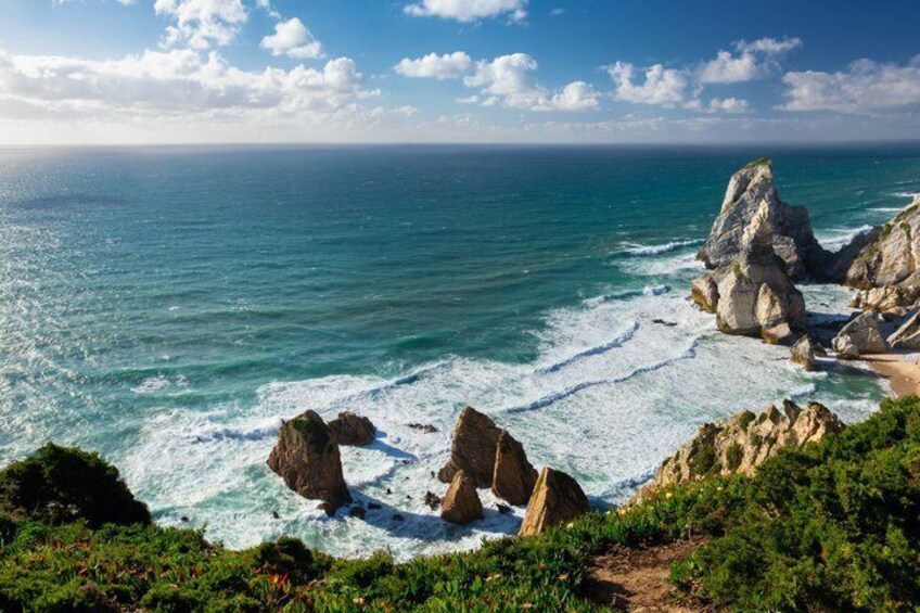 A coastal landscape with large rock formations, a sandy beach, and the ocean. 4