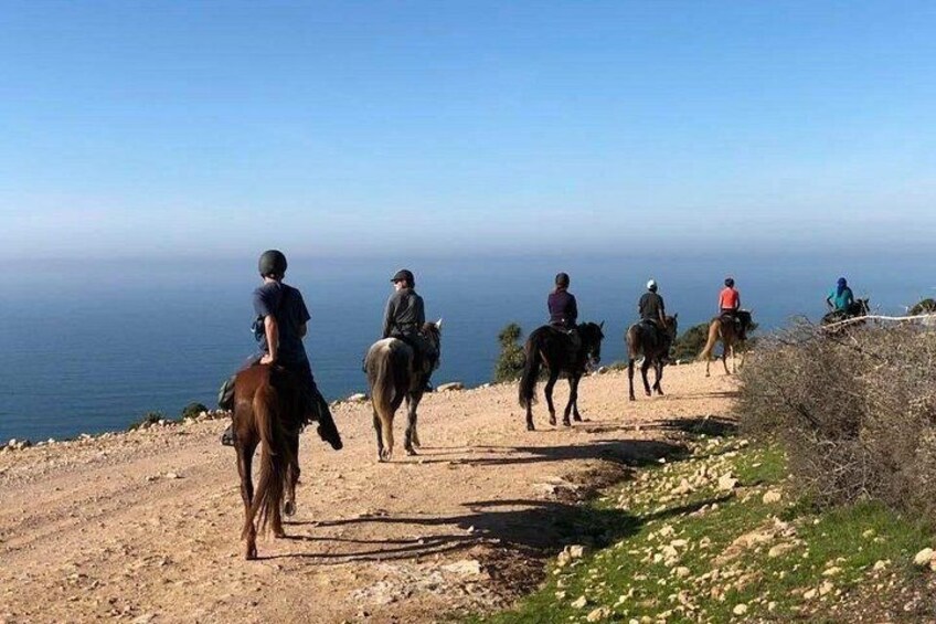 A group of people horseback riding on a dirt path with a view of the ocean. 2