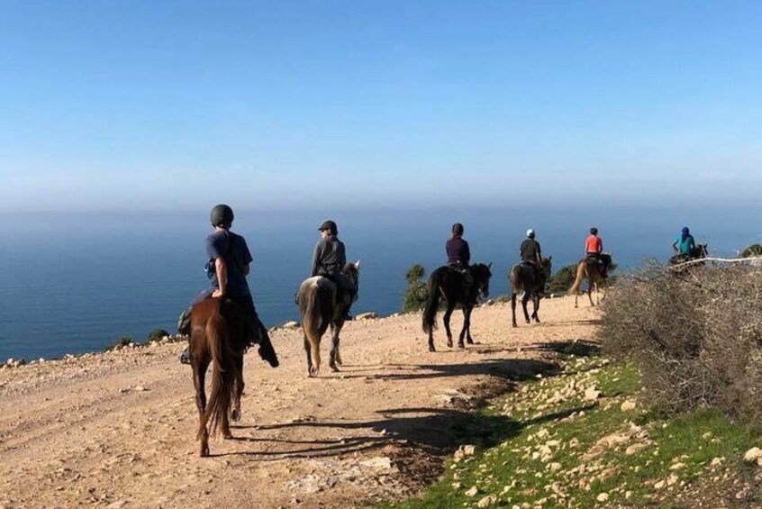 A group of people horseback riding on a dirt path with a view of the ocean. 2