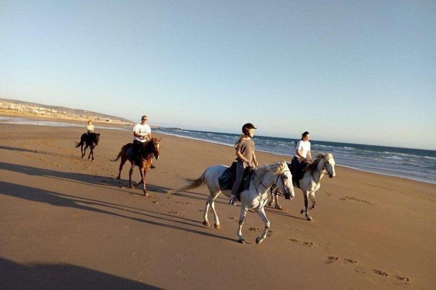 A beach with people riding horses. 2