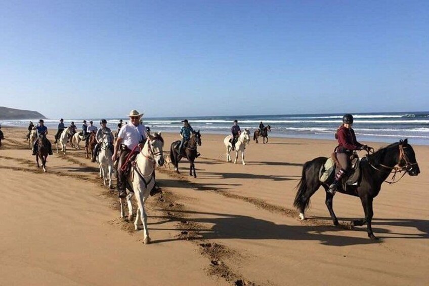 A group of people riding horses along a sandy beach with the ocean in the background. 3