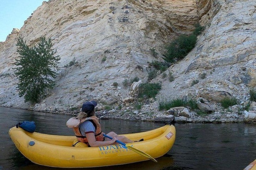 A person in a yellow inflatable raft on a calm river, surrounded by rocky cliffs. 2