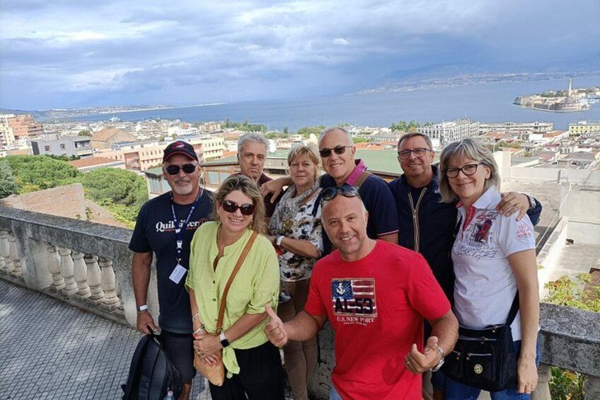 A group of people standing on a balcony overlooking a cityscape with a body of water in the distance. 1