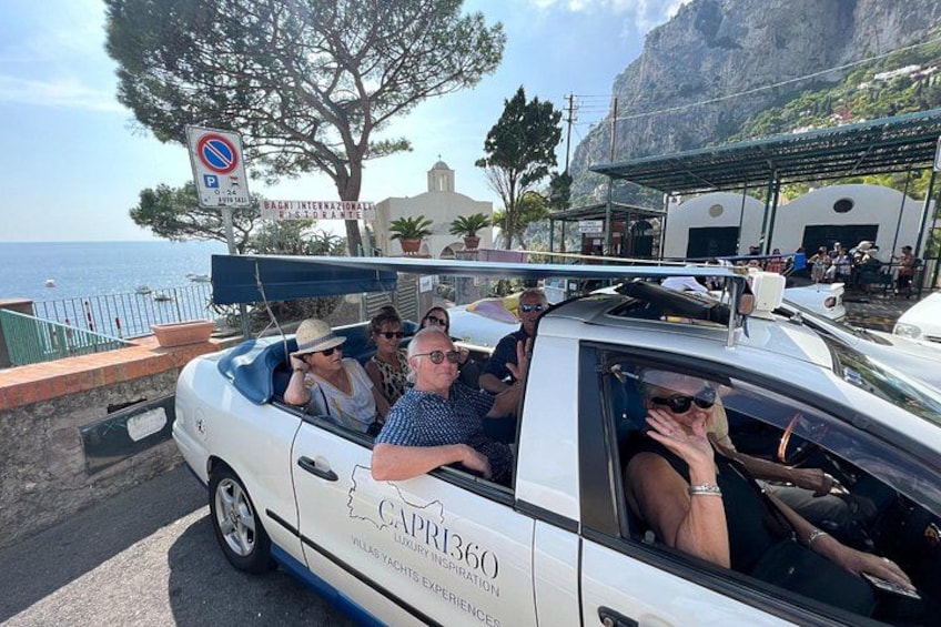 A white convertible car with passengers, parked near a coastal area with a sign indicating no parking. 4