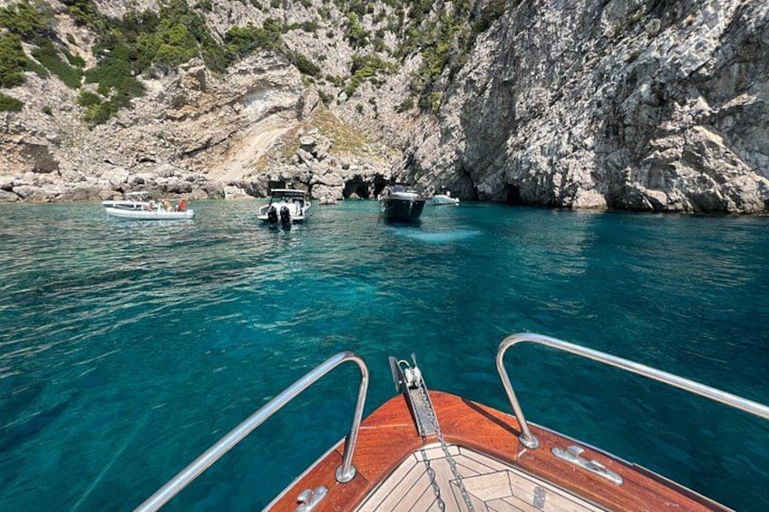 A boat's deck with clear turquoise water, rocky cliffs, and other boats in the background. 2