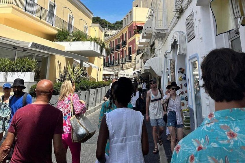 A crowded street with people walking, buildings with balconies, and a white storefront with decorative items. 3