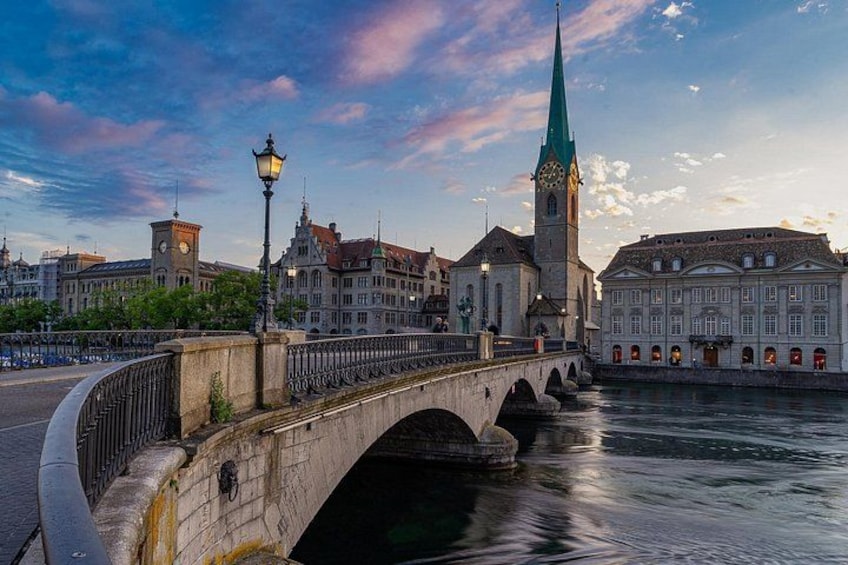 Eine Steinkonstruktion überspannt einen Fluss, ein Glockenturm und historische Gebäude sind zu sehen. 5