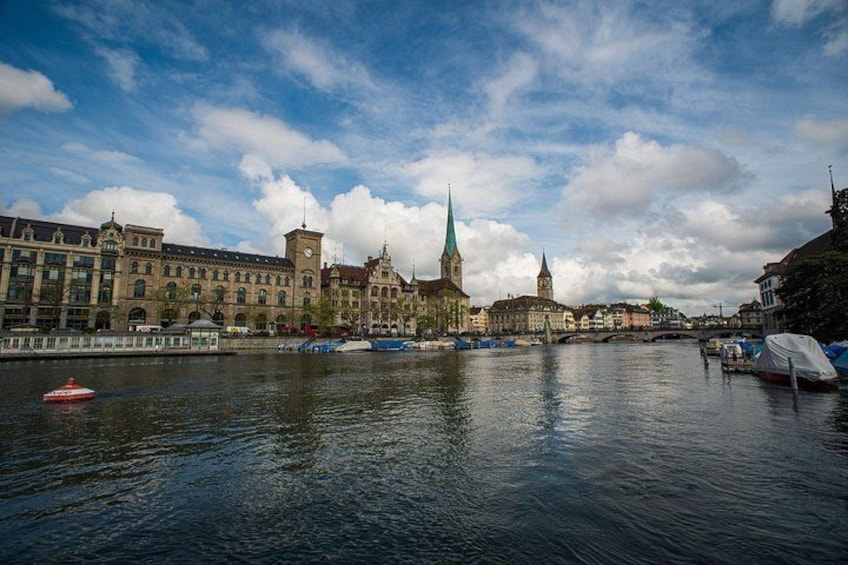A river with boats, a church with a green spire, and historic buildings along the riverbank. 1