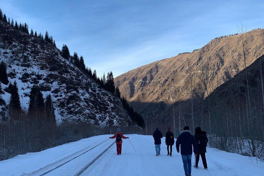 A snowy road with people walking, surrounded by mountains and trees. 5