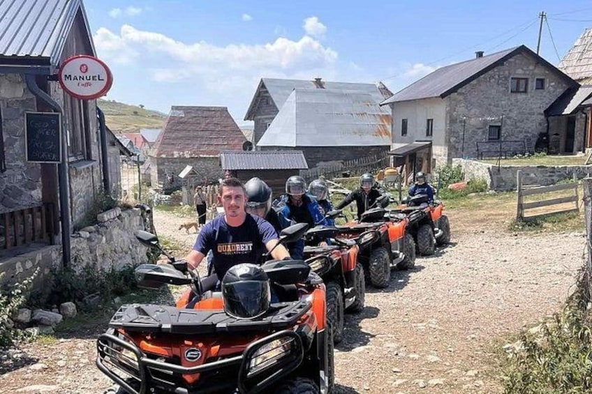 A group of people on ATVs in a rural setting with stone buildings and a dirt road. 5