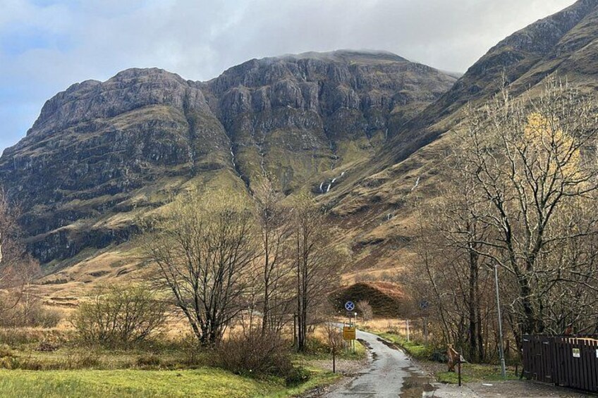 A mountainous landscape with a winding road, leafless trees, and a distant waterfall. 3