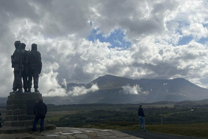 A statue of two figures on a pedestal, a mountain in the background, and a cloudy sky. 3