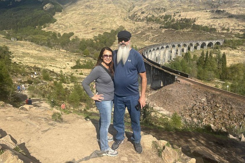A man and a woman standing on a rocky outcrop with a railway viaduct in the background. 2