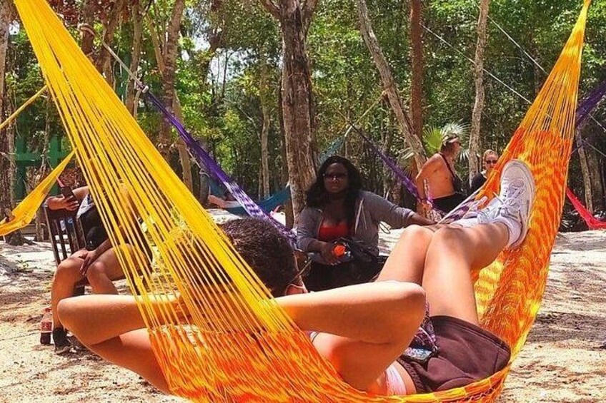 Une personne se détend dans un hamac jaune sur une plage de sable, avec des arbres en arrière-plan. 3