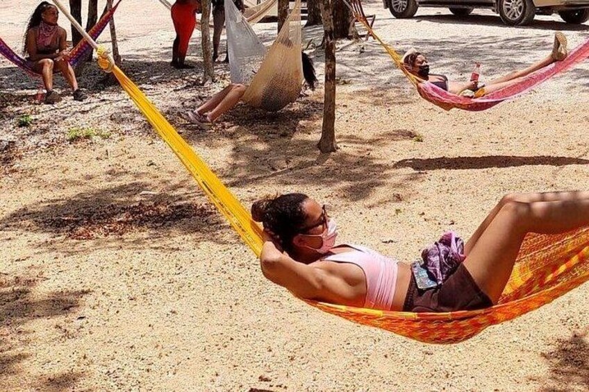 Une personne se détend dans un hamac, posé sur du sable, avec des arbres et un véhicule garé en arrière-plan. 2