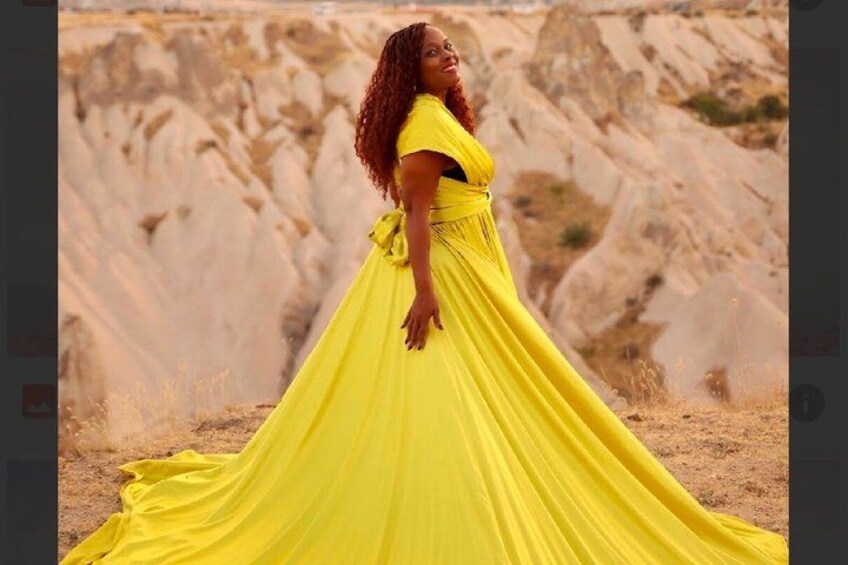 A person in a flowing yellow dress standing in a desert landscape with rocky formations. 2