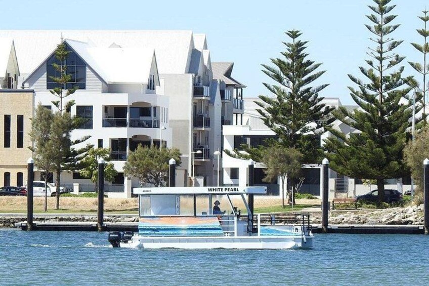 Un barco llamado 'WHITE PEARL' en una masa de agua con edificios modernos y árboles al fondo. 2