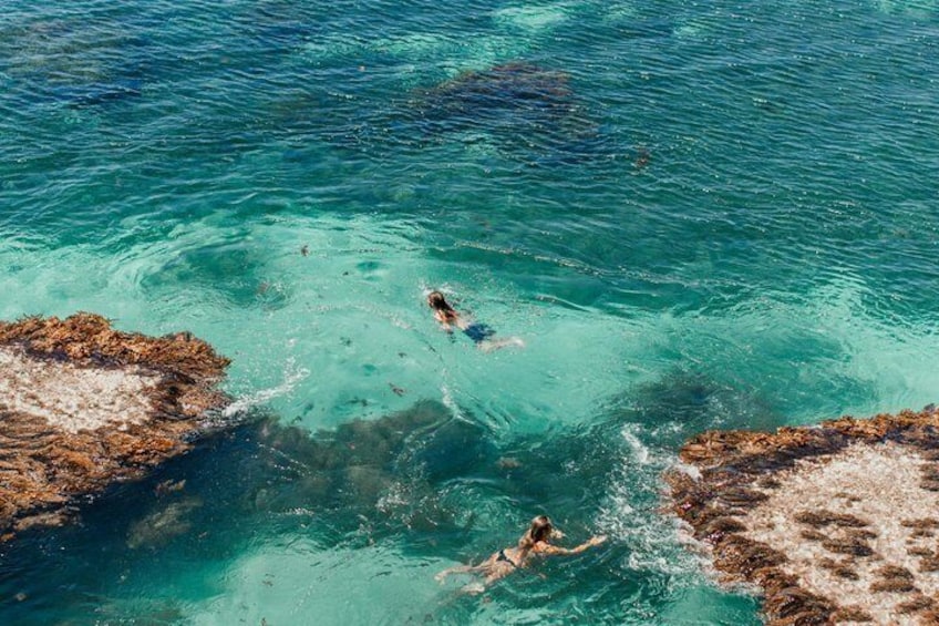 Two people swimming in clear turquoise water with rocky formations. 2