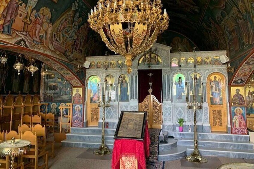 An ornate church interior with a large chandelier, religious icons, and a red altar cloth. 5