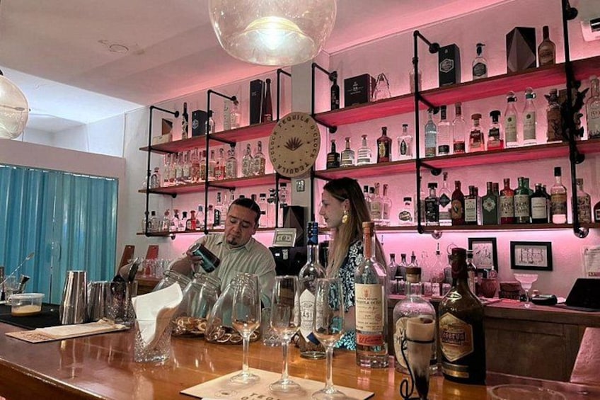 Un bar con estantes llenos de botellas y una persona sirviendo una bebida. 4