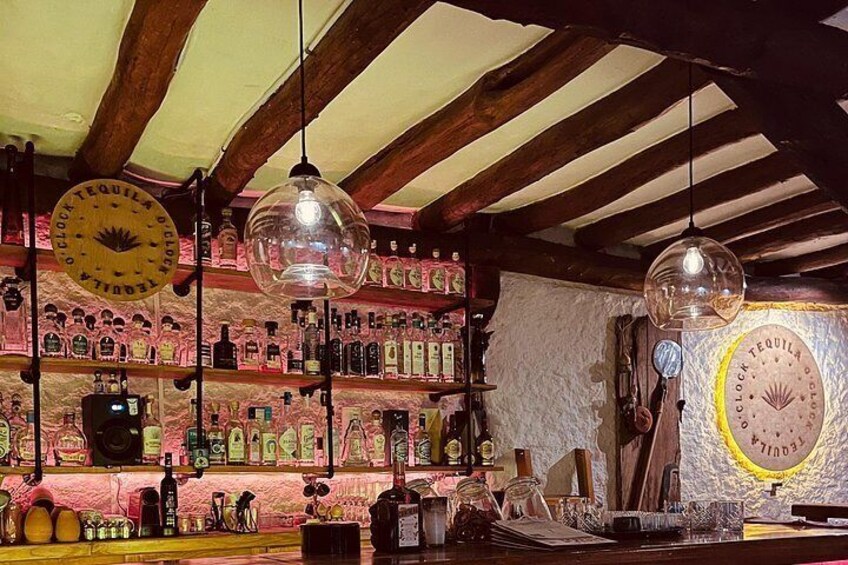 Un bar avec des poutres en bois, des globes en verre suspendus et des étagères remplies de bouteilles d’alcool. 3