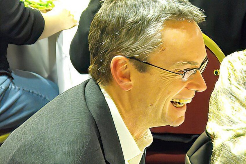 A person wearing a grey suit and glasses, seated in a vehicle. 2