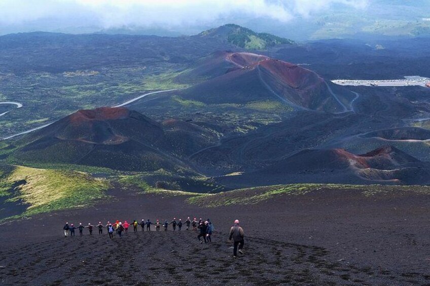 En gruppe mennesker vandrer i et vulkanlandskab med tydelige røde og grønne områder. 3