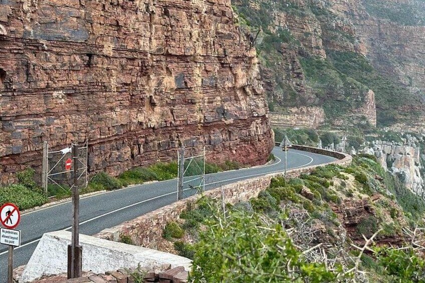 A winding mountain road with guardrails, a no-entry sign, and a rocky cliff face. 2