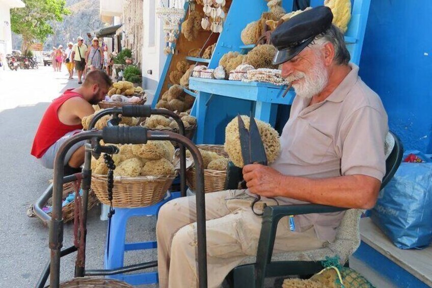 A man sitting on a chair at a street stall selling various items. 1
