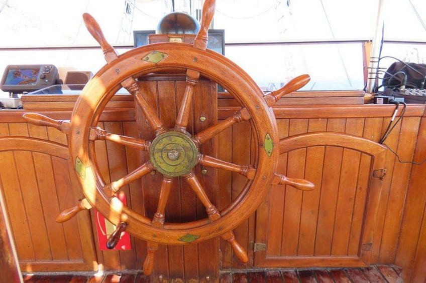 A wooden ship's wheel with a brass center, surrounded by a wooden deck with a railing. 3