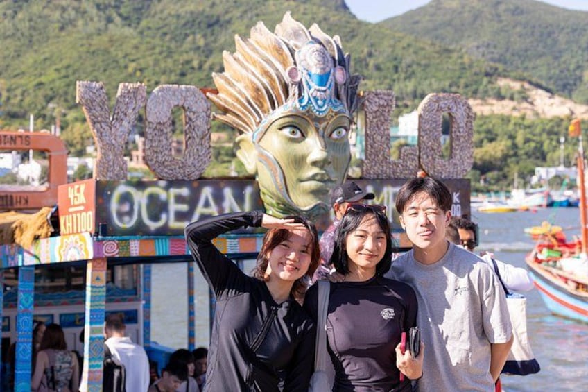 Un grupo de personas posando frente a un letrero con un rostro grande y el texto 'YOLO OCEAN'. 3