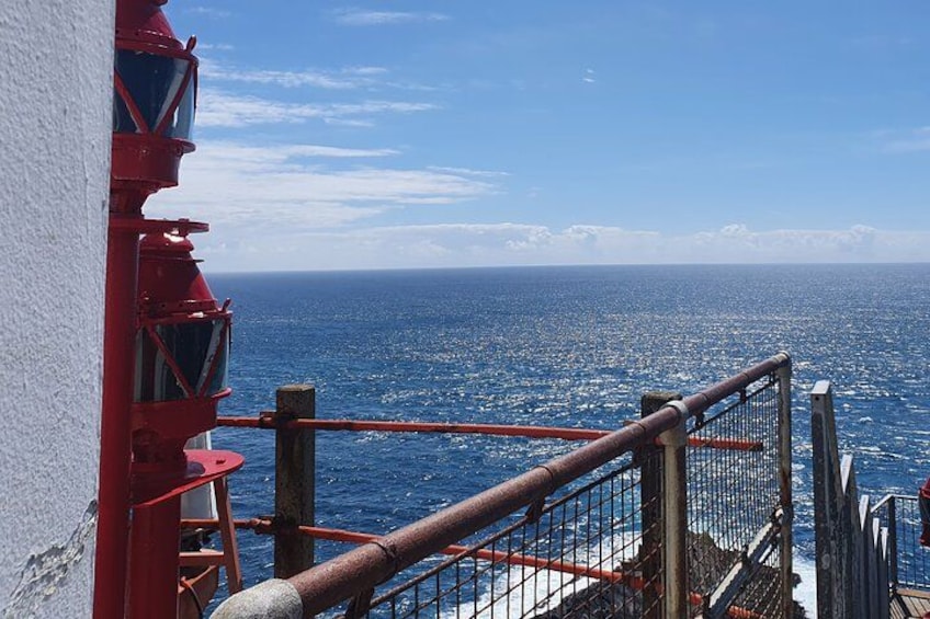 Una estructura roja de faro, una barandilla de metal y el océano. 3