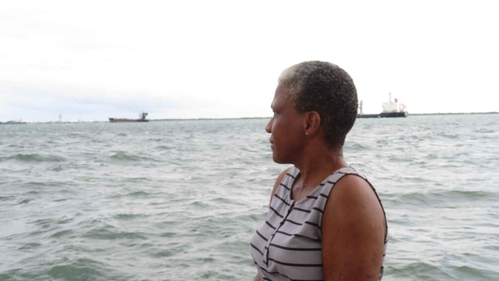 A person standing on a boat with a ship in the background. 1